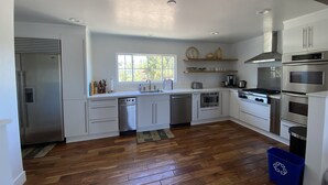Een moderne keuken met witte kastjes, roestvrijstalen apparatuur, een houten visgraatvloer en een raam dat natuurlijk licht binnenlaat.