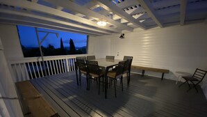 Een overdekt terras met een eettafel en stoelen, een bankje, en uitzicht op de avondhemel.