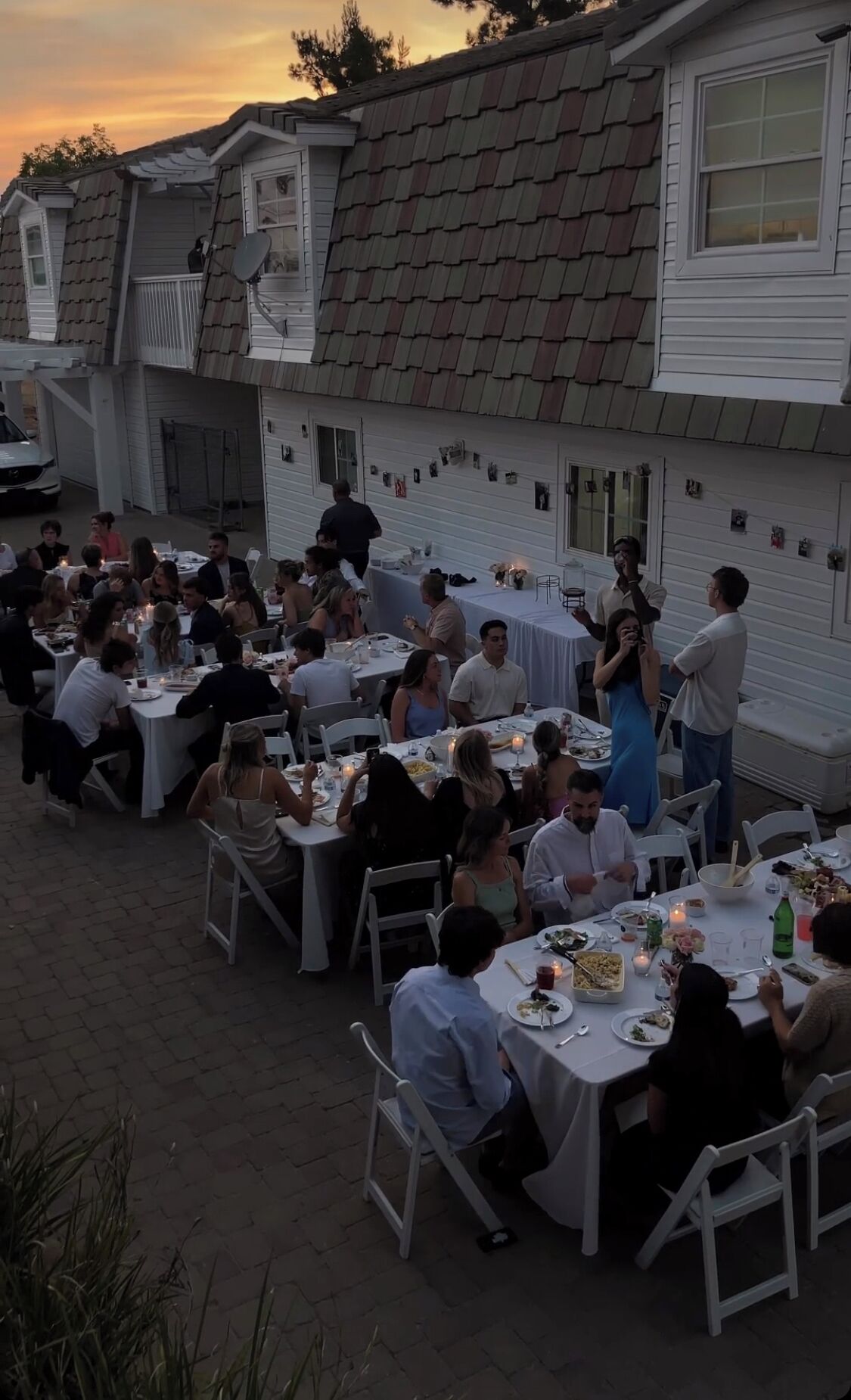 Un área de comedor al aire libre con mesas y sillas, rodeada por un edificio con techo inclinado.