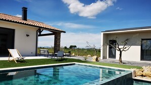 A swimming pool with clear blue tiles, a covered patio with chairs, and a view of the countryside. - Villa with exceptional 4-star certified viewSPA and heated infinity pool (Servian)