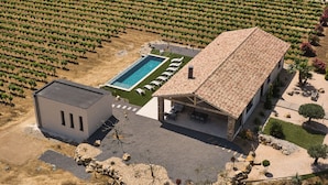 An aerial view of a vineyard with rows of grapevines, a swimming pool, and a building with a tiled roof. - Villa with exceptional 4-star certified viewSPA and heated infinity pool (Servian)