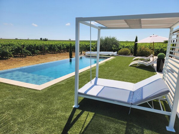 A poolside area with a covered seating area, a pool, and a view of a vineyard.