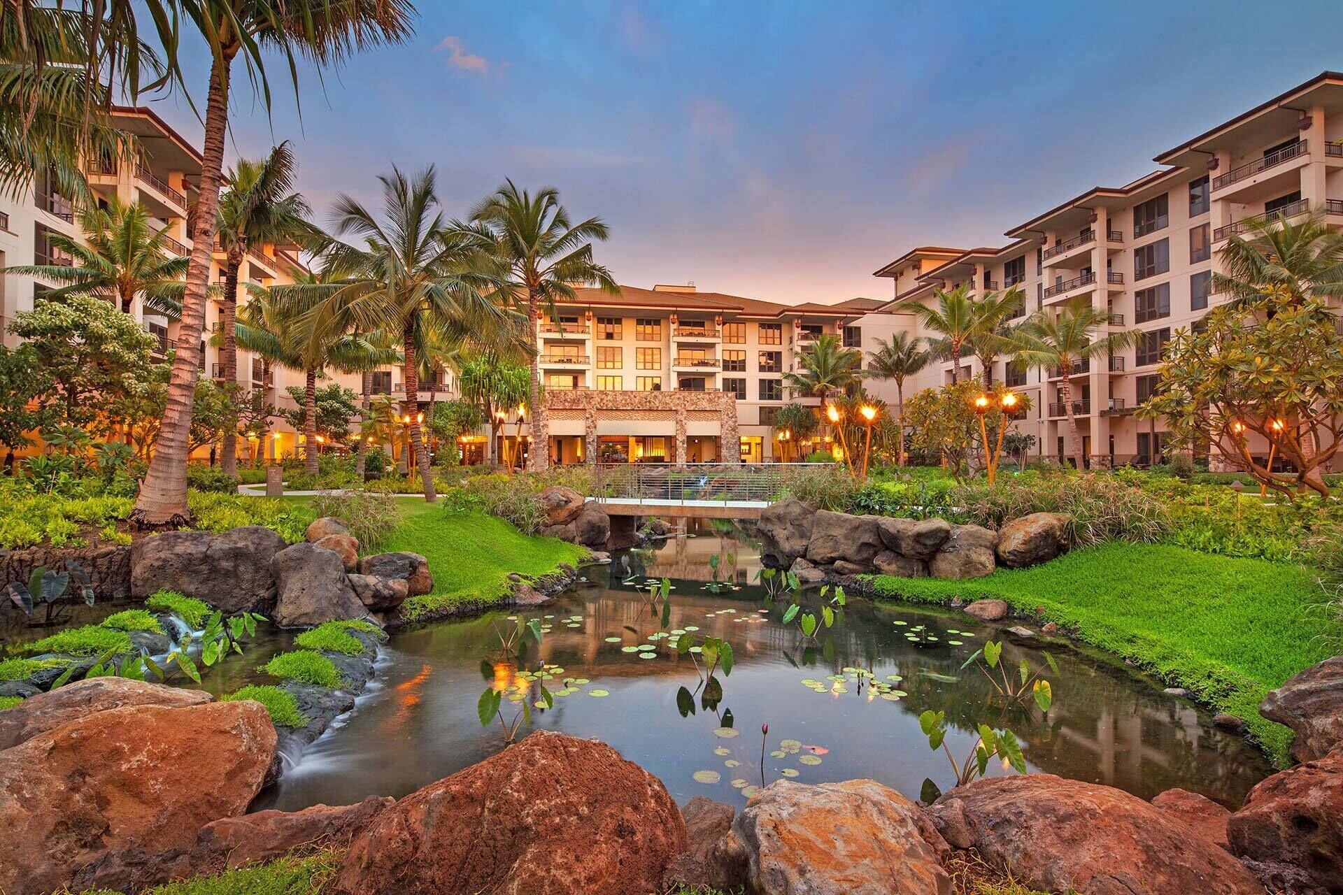A hotel with multiple floors, a central courtyard with a small pond, and surrounding greenery.