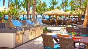 An outdoor dining area with thatched umbrellas, wicker furniture, and a barbecue station. - Westin Nanea - Beautiful Resort On The Beach! Family Friendly Resort (Lahaina)