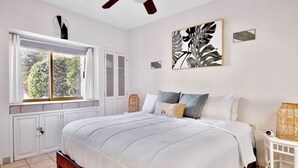 Ein Schlafzimmer mit einem Bett, einem Fenster mit Rollläden, einem Deckenventilator und einem an der Wand hängenden Kunstwerk.