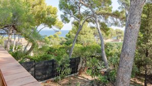A coastal property with a wooden deck overlooking a sea view, surrounded by dense pine trees and a black metal fence. - Marysol by Interhome (Les Issambres)