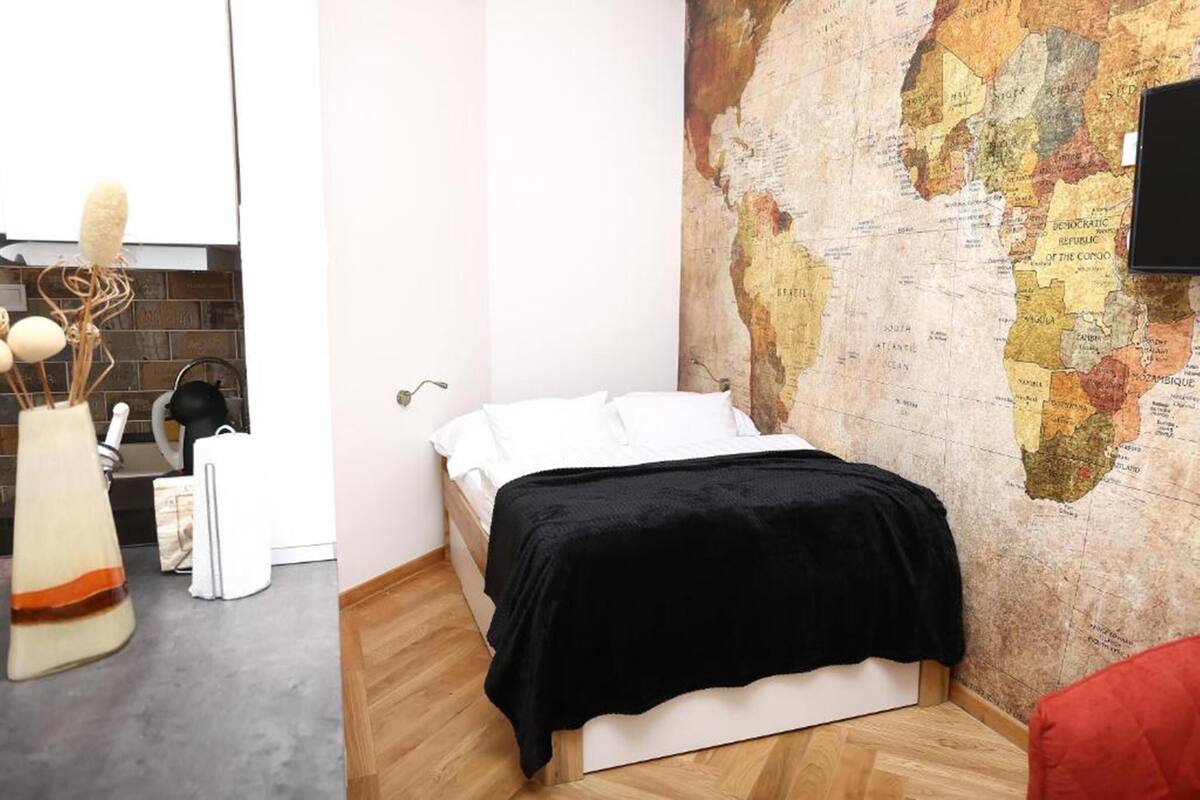 A bedroom with a bed, a map on the wall, and a kitchen area with a stove and cabinets.