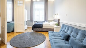 A modern bedroom with a bed, a blue sofa, a round rug, and a window with curtains. - Central Luxury Apartment (Budapest)