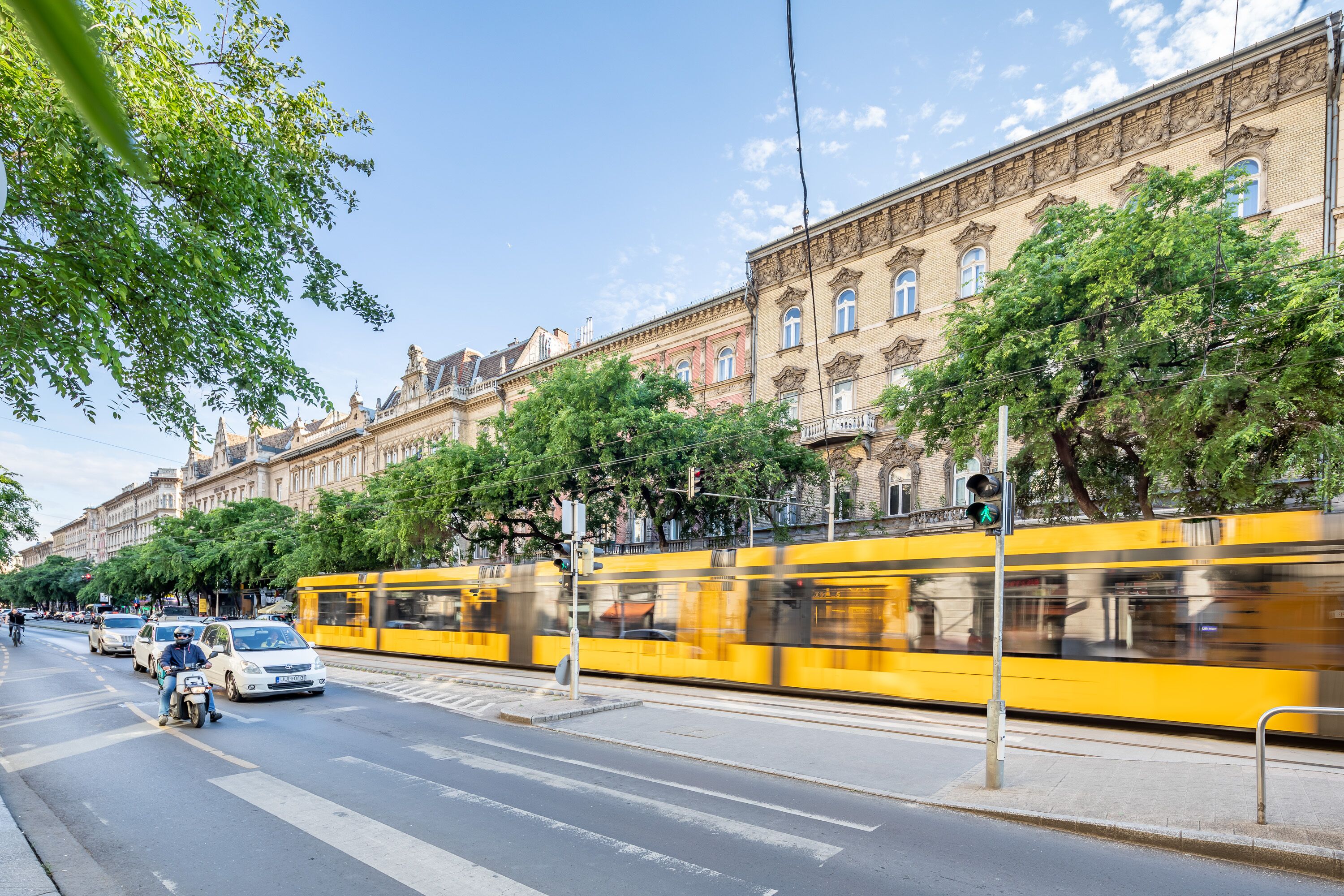 A tram moving along a street with buildings and trees.