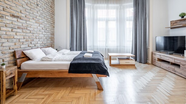A modern bedroom with a brick wall, a wooden bed, a TV, and a small table. - Central Luxury Apartment (Budapest)