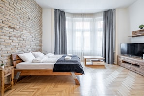 A modern bedroom with a brick wall, a wooden bed, a TV, and a small table. - Central Luxury Apartment (Budapest)