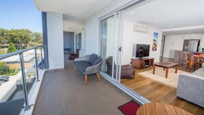 A modern apartment with a balcony, a living area with a sofa and TV, and a kitchen area. - Shore Thing - Shoal Bay (Shoal Bay)