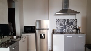 Una cucina compatta con frigorifero in acciaio inox, forno a microonde, erogatore d'acqua e decorazioni sulla parete a mosaico.
