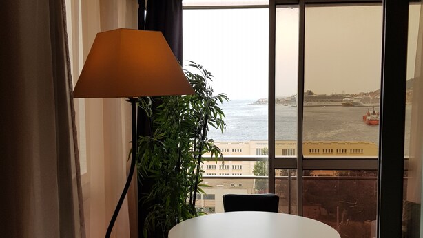 Un balcone con tavolo e sedie, una pianta in vaso e vista sul mare e sugli edifici.