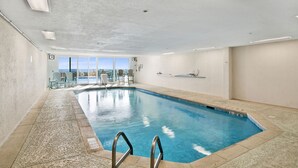 Una piscina interior con paredes de vidrio transparente, suelo de baldosas y vistas al horizonte de la ciudad.