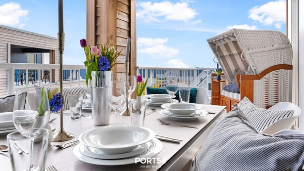 Een eetgedeelte met een tafel voor vier personen, een rieten stoel en uitzicht op zee.