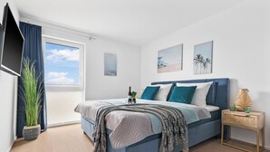 Een slaapkamer met een bed, nachtkastje, lamp en raam met gordijnen.