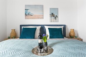 Un lit avec une couverture à motifs, deux oreillers, une bouteille de vin et un vase rempli de fleurs, le tout posé sur un plateau.
