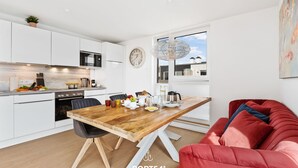 Een moderne keuken met witte kasten, een houten eettafel en een rode bank.