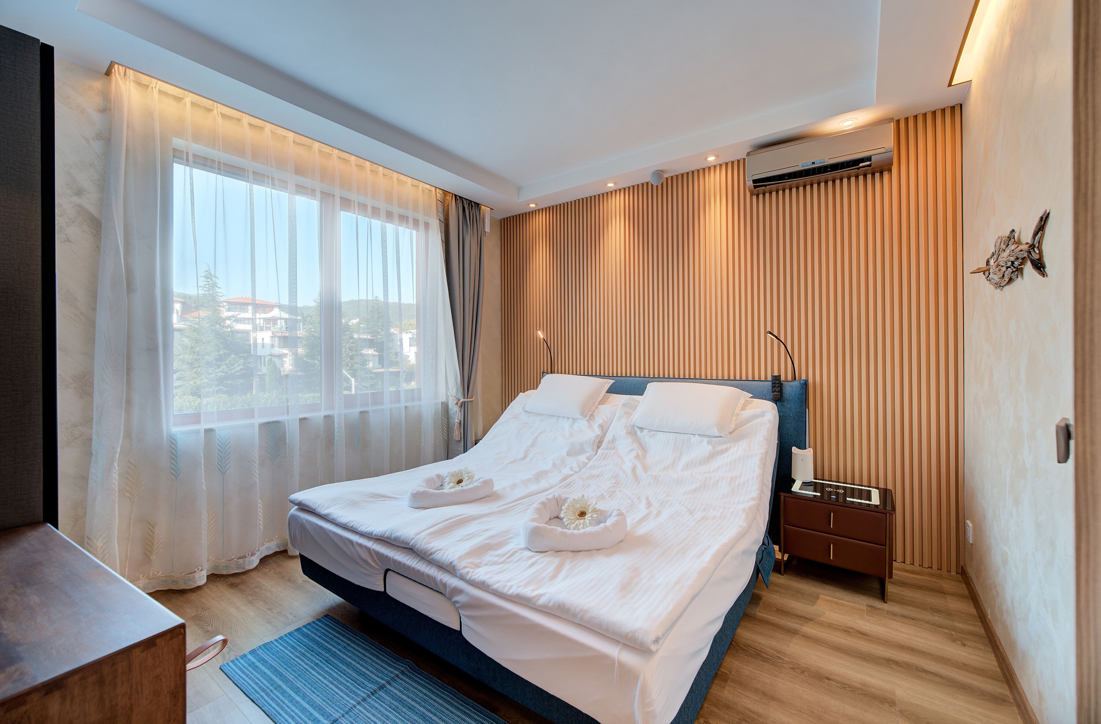 Een moderne hotelkamer met een groot bed, nachtkastje en een raam met dunne gordijnen.