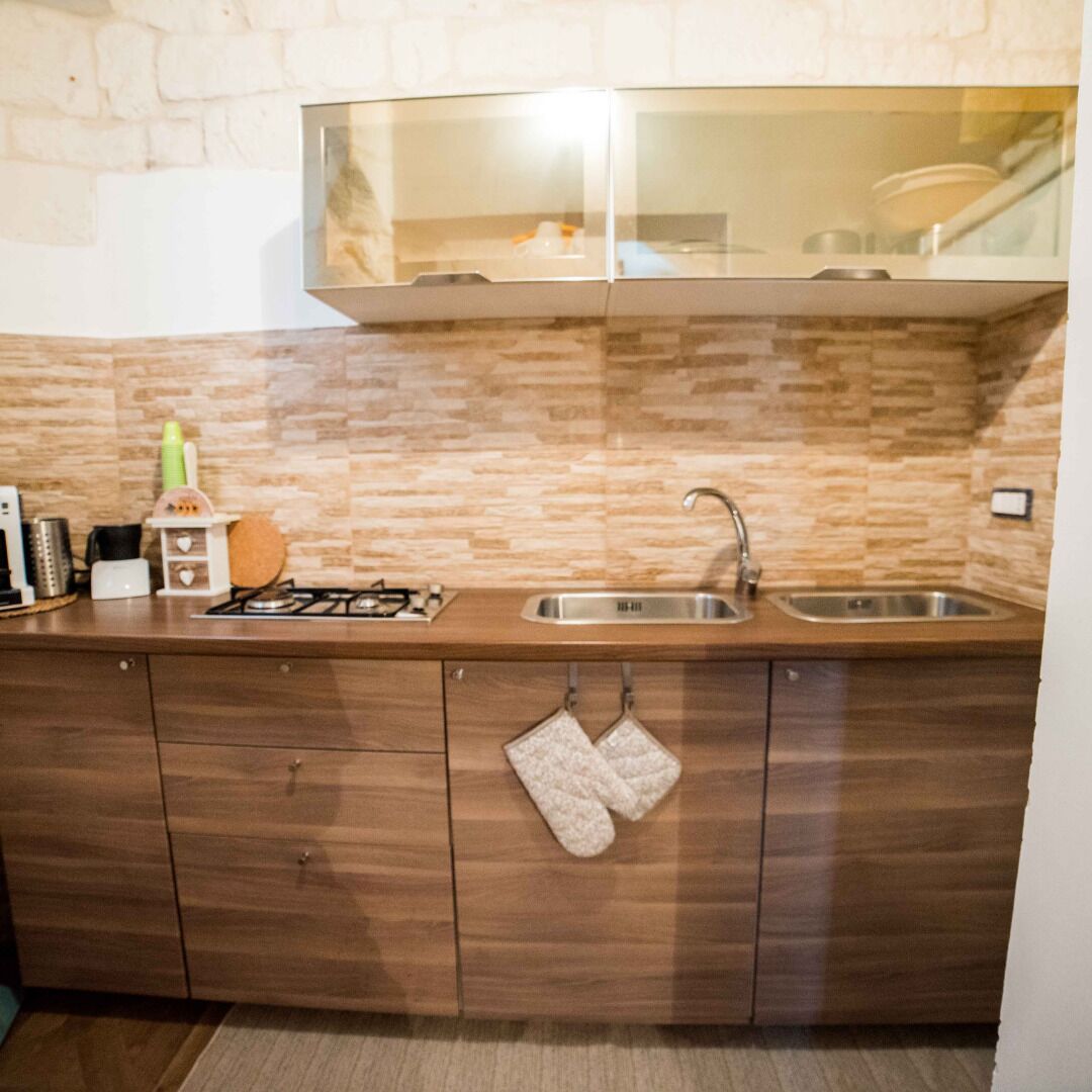 A kitchen with a stone backsplash, wooden cabinets, a stainless steel sink, and a gas stove.
