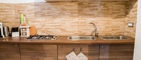 A kitchen with a stone backsplash, wooden cabinets, a stainless steel sink, and a gas stove.