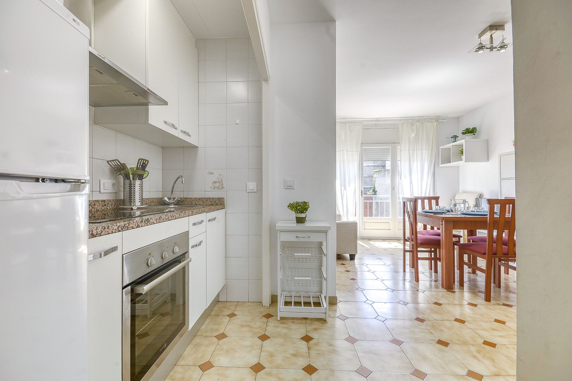 Een keuken met witte kastjes, een granieten aanrecht, een fornuis en een spoelbak. Er is een eethoek met houten stoelen en een tafel.