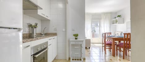 Een keuken met witte kastjes, een granieten aanrecht, een fornuis en een spoelbak. Er is een eethoek met houten stoelen en een tafel.