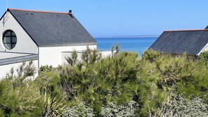 A coastal house with a grey roof, a circular window, and a view of the sea.