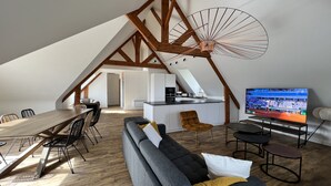 A modern loft apartment with a dining area, a living room with a sofa and TV, and a kitchen.