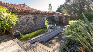 A stone building with a tiled roof, a wooden deck, and a small water feature. - Spacious family lodge with natural pool, near Nantes (La Limouzinière)