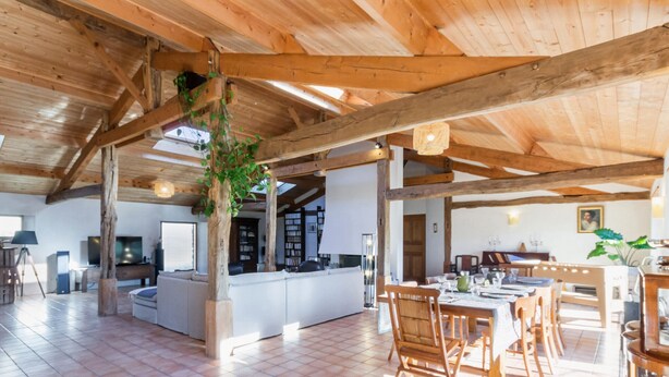A spacious open-plan living area with a high ceiling, wooden beams, and a tiled floor. - Spacious family lodge with natural pool, near Nantes (La Limouzinière)