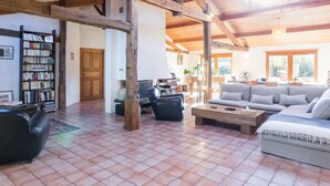 A spacious living area with a high ceiling, wooden beams, a large sofa, a coffee table, and a bookshelf. - Spacious family lodge with natural pool, near Nantes (La Limouzinière)