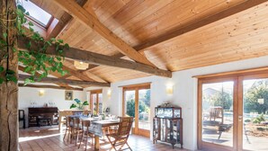 A spacious dining area with a wooden ceiling and tiled floor, a piano, and a large window overlooking a garden. - Spacious family lodge with natural pool, near Nantes (La Limouzinière)