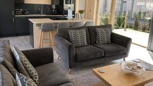 Ein modernes Wohnzimmer mit einer Couch, einem Couchtisch und einer Küchenzeile mit einer Uhr, Barhocker und einem Esstisch.