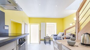 A modern kitchen with a stove, microwave, and cabinets, leading to a dining area with a table and chairs. - Charming Cottage near River & Park, 10km from Nantes, Free Parking, WiFi, Baby-Friendly (Vertou)