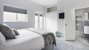 A modern bedroom with a large bed, a walk-in closet, and a bathroom with a towel rack. - Oceanwalk - sleeps 8 guests  in 4 bedrooms (Perranporth)