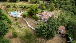 Vista aérea de una propiedad con piscina, una casa de piedra con tejado de tejas y follaje circundante.