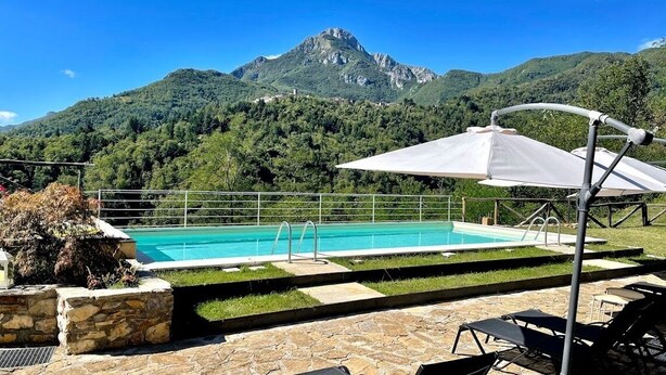 Zona de piscina con vista a la montaña, escalones de piedra y mobiliario exterior.
