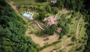 Luftaufnahme eines Anwesens mit Schwimmbad, einem Gebäude mit rotem Dach und umliegender Bepflanzung.