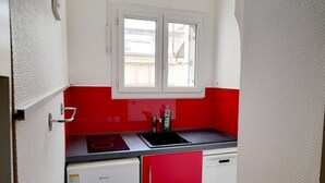 A compact kitchen with a red and white color scheme, a window, a sink, a stove, a refrigerator, and a dishwasher.