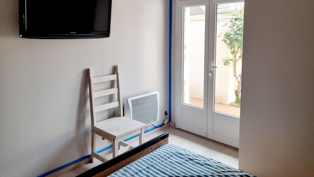 A room with a bed, a chair, a television mounted on the wall, and a sliding glass door leading to an outdoor area.