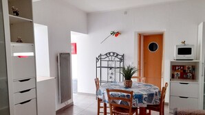 A dining area with a table, chairs, a potted plant, a radiator, and a TV on a shelf.