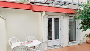 A patio with a white table and chairs, a red awning, and a sliding glass door.