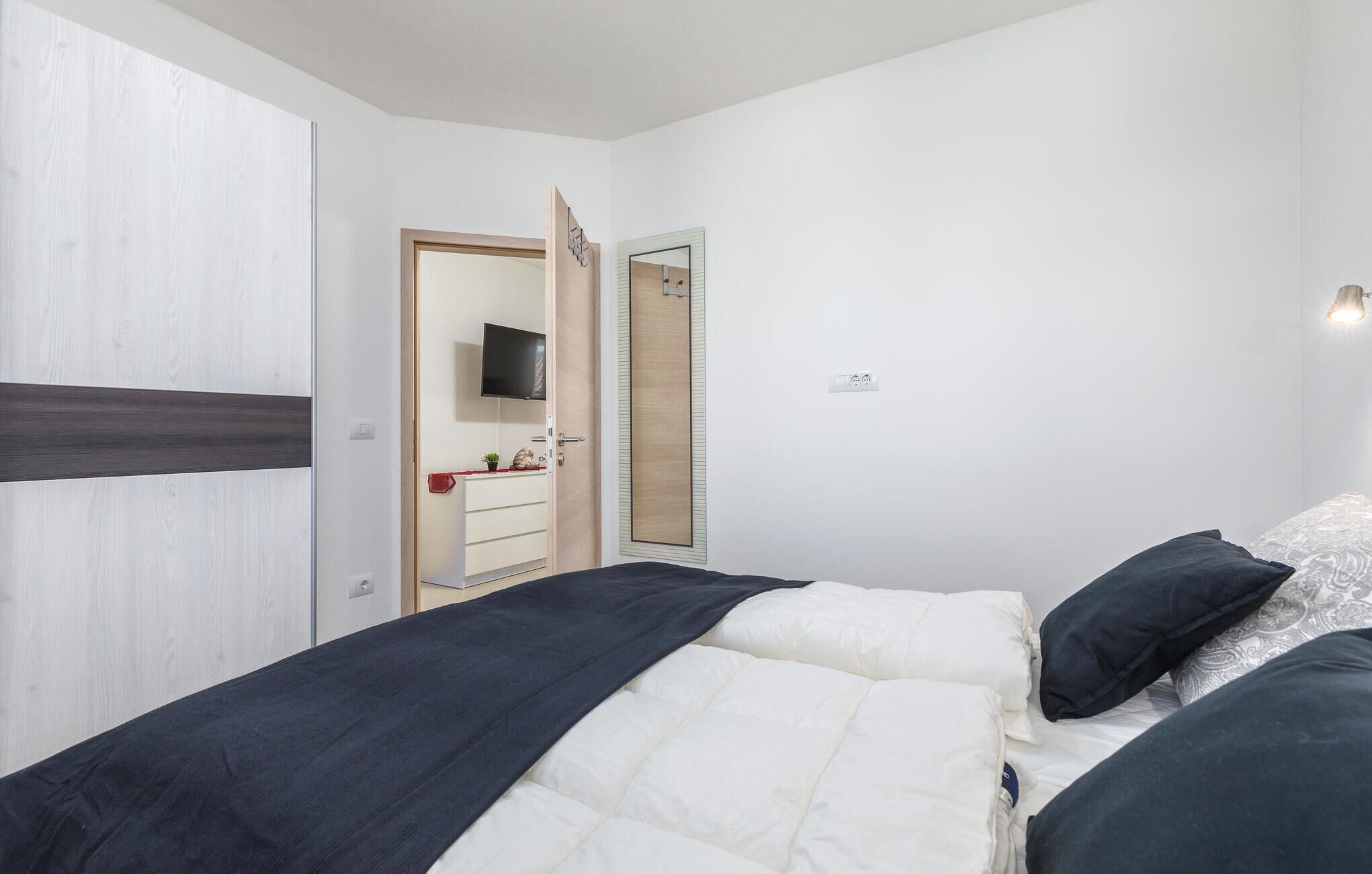 A bedroom with a bed, a dresser, a television, and a mirror.