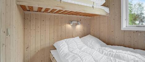 A bedroom with a bunk bed, wooden walls, a window with a view of trees, and a wall-mounted light fixture.