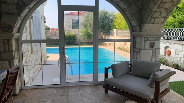 A room with a stone wall, a large window overlooking a swimming pool, and a cushioned bench.