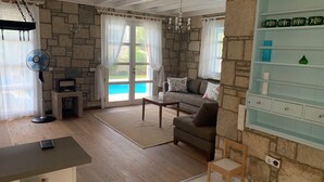 Ein Wohnzimmer mit Steinwand, einer Couch, einem Couchtisch, einem Ventilator und Blick ins Freie.
