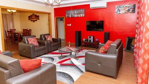 Ein Wohnzimmer mit Ledersofas, einem Glastisch, einem Flachbildfernseher und roten Wänden.