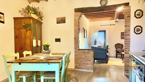 A dining area with a wooden table and chairs, a cabinet with plants, and a view of a living room through an archway.